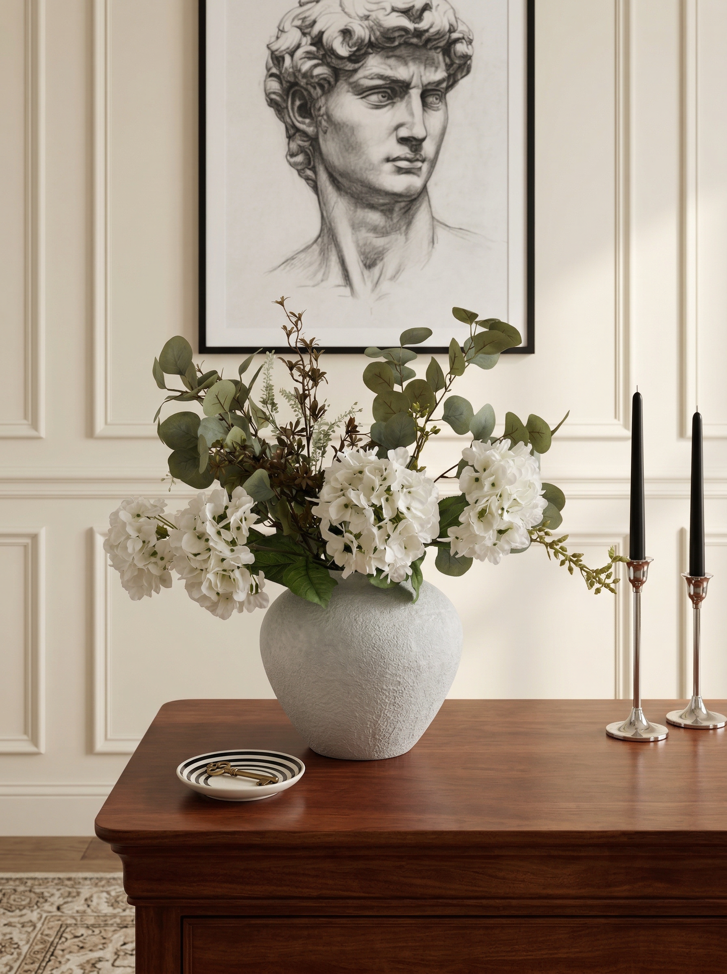 Decorative vase with flowers on a wooden table against a wall with a framed portrait.