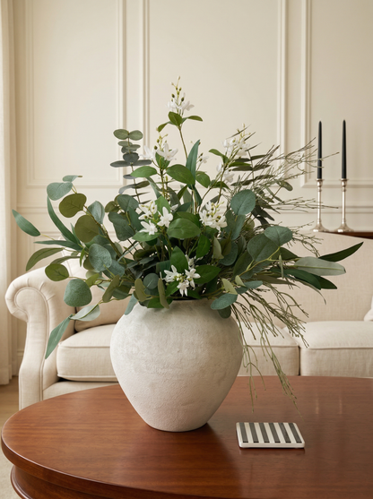 Decorative plant arrangement in a white vase on a wooden table with a neutral background