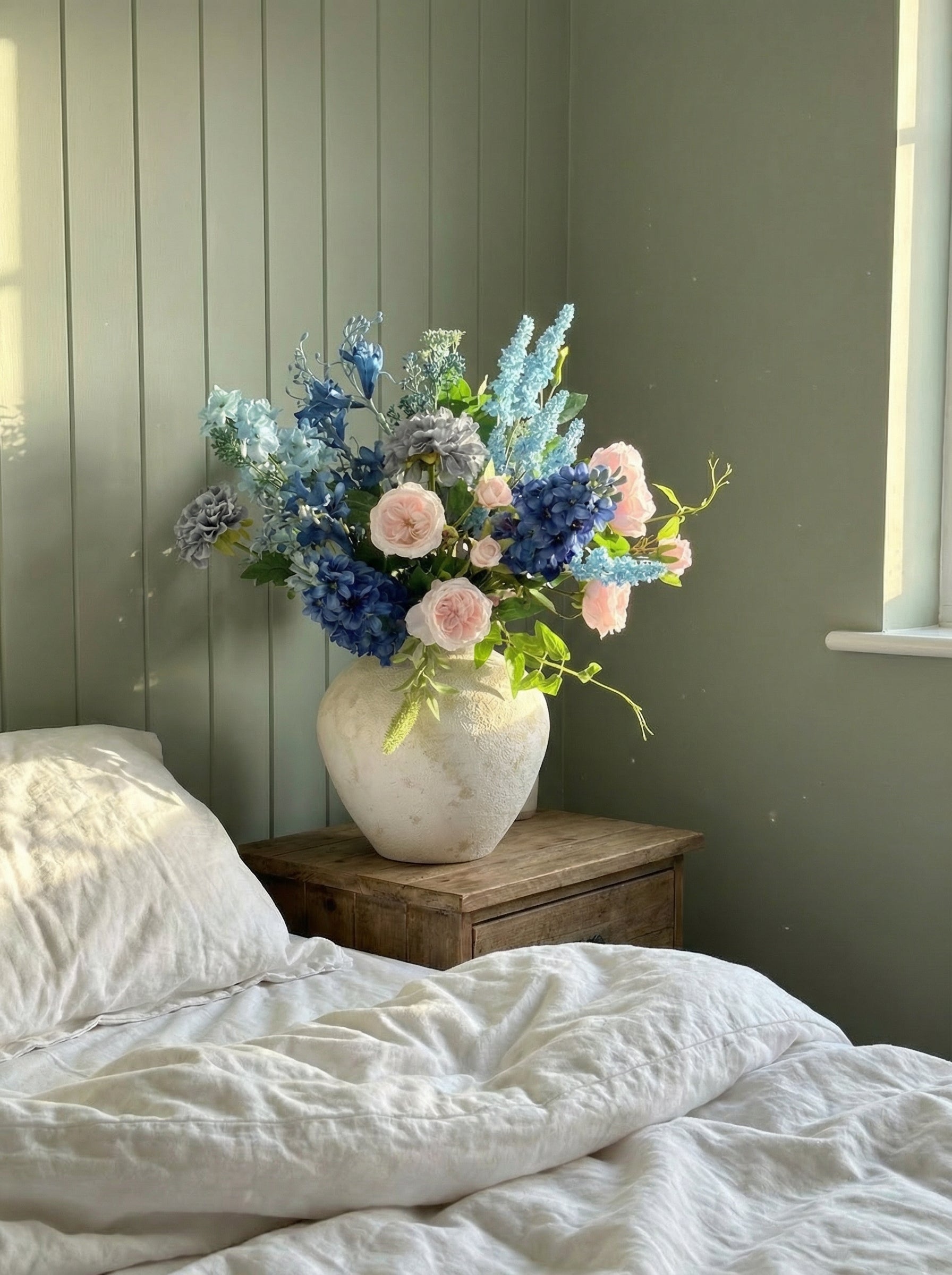 Vase of flowers on a bedside table with a bed in the foreground