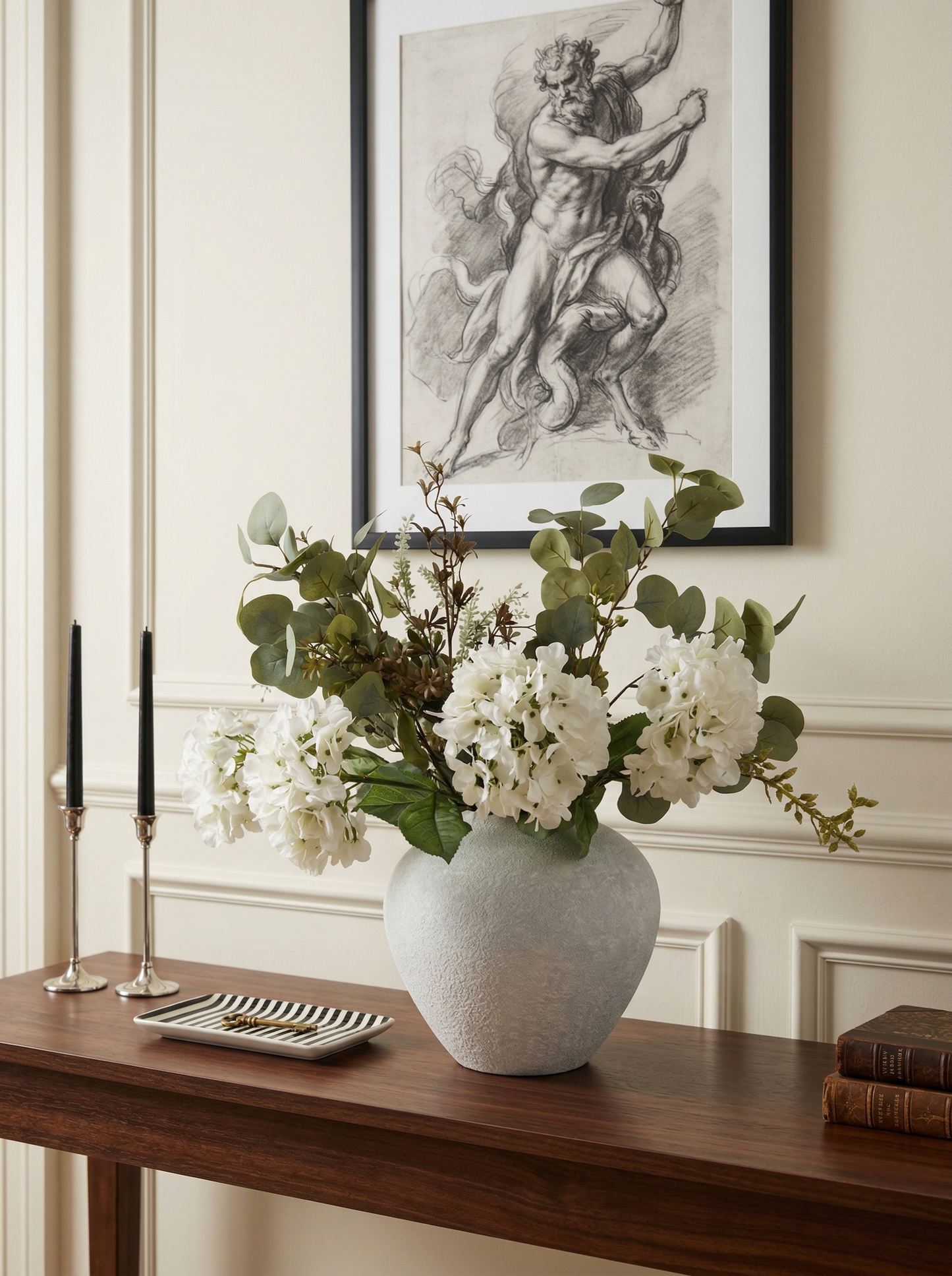 Vase with white flowers on a wooden table in a room with a framed artwork on the wall.
