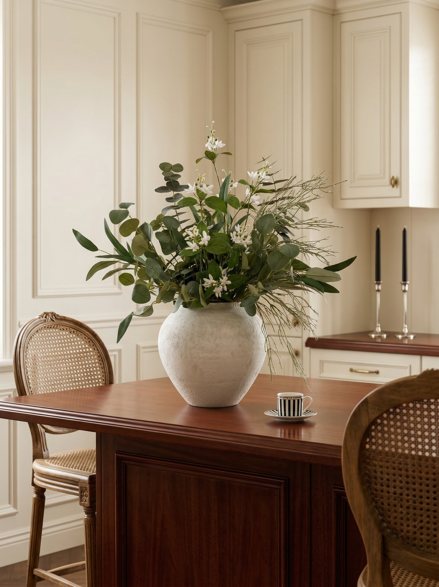 White vase with greenery on a wooden table in a kitchen setting